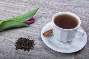 A cup of tea with cinnamon and purple tulips