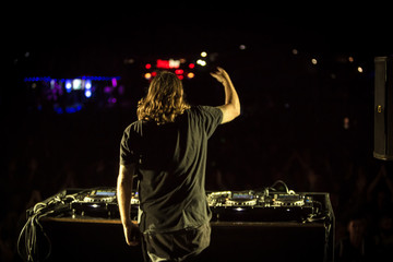 DJ with headphones at night club party under the colorful light and people crowd in background. Dj at open aire party. Night party at sea coast. Beach party.