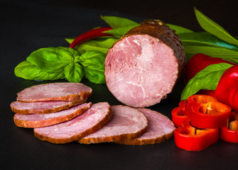 Smoked sausage, ham with red and green peppers and herbs on a dark background
