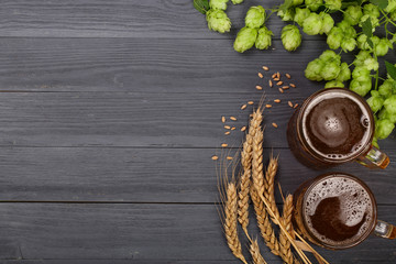 glass of foamy beer with hop cones and wheat on black wooden background. Top view with copy space for your text