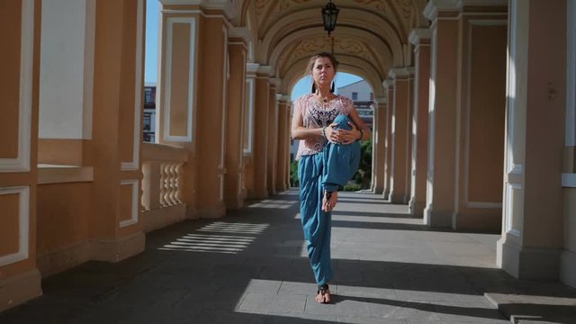 Beautiful girl in blue pants and pink lace top walking in historic architecture. Yoga in the city. Health concept. Slow motion. Woman goes to the camera and smiling.
