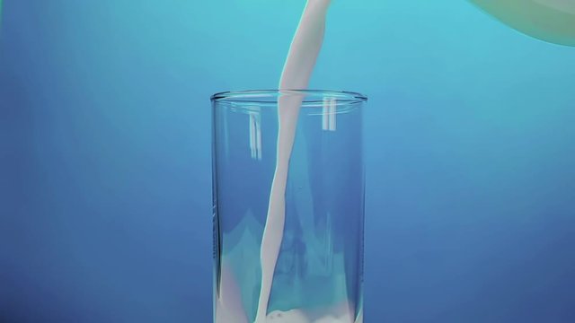fresh white milk pouring into drinking glass on blue background, shooting with slow motion, diet and healthy nutrition concept