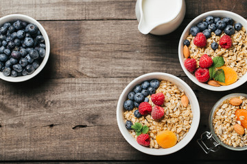 Homemade granola and healthy breakfast ingredients - milk, dried fruit and berries on wooden background