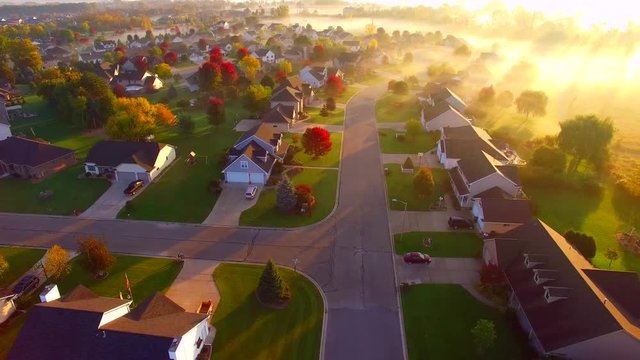 Tranquil idyllic Autumn neighborhood houses shrouded in fog at daybreak, Fall colors, aerial flyover.