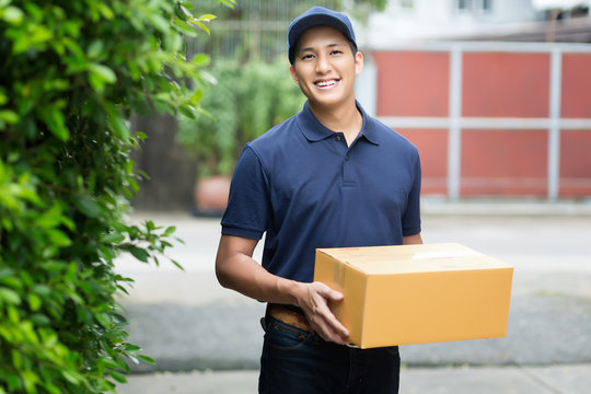 Young asian delivery man smiling while holding a cardboard box delivery to his customer.