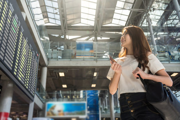 Asian woman traveler holding the passport at the flight information screen in modern an airport, lifestyle travel and transportation concept.