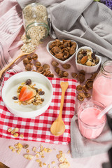 Obraz na płótnie Canvas Breakfast set. Strawberry fruit over the yogurt in white bowl with Oat granola and nuts on teble set background, serve with pink milk in Bottle, top view, Healthy food concept