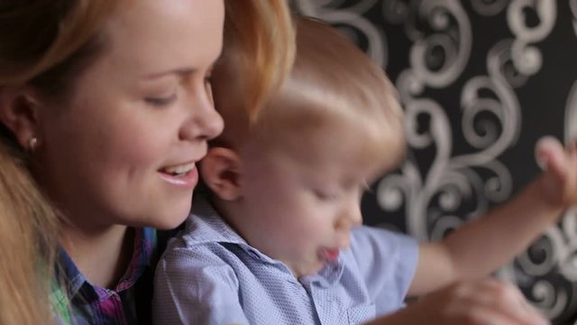 Young mother and her emotional son playing with plasticine while sitting at table.