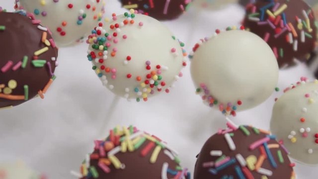 Dessert balls with chocolate icing decorated with colorful confetty on sticks stuck in styrofoam