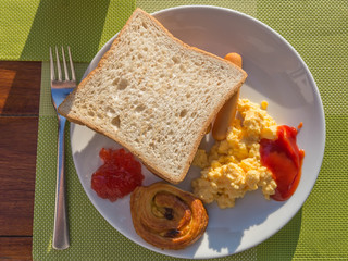 western breakfast, toast, scrambled egg, sausage, and pastry on white plate
