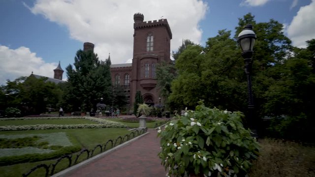 Steadicam shot walking through the gardens of the Smithsonian Institutions Castle Museum on a beautiful late spring day with blue sky and white clouds.