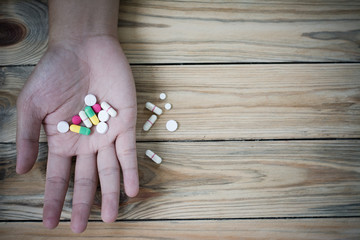 Medicine pills and capsules in hand on wooden background