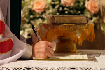 Fototapeta na wymiar Priest is signing significant document for wedding ceremony in church