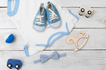 baby bodysuit with blue shoes and baby toys on wooden background. Flat lay