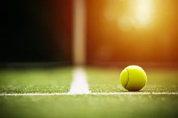 Poster Weicher Fokus des Tennisballs auf Tennisrasenplatz mit Sonnenlicht © kireewongfoto