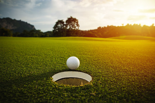 selective focus. white golf ball near hole on green grass good for background with sunlight and lens flare effect