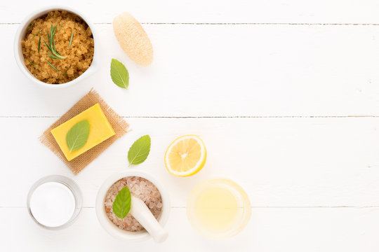 Homemade skin care and body care with natural ingredients salt, mint, rosemary, lemon, oil, luffa, natural lotion set up on white wooden background.