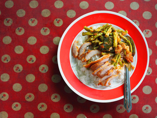 Top view deep fried crispy slice cut pork and Thai local spicy stir fried string bean, chili paste, and pork belly, on Jasmine rice, red melamine plastic plate, white dot cherry pattern 