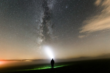 Obraz na płótnie Canvas Mensch leuchtet mit Taschenlampe Nachts zur Milchstraße, Sternenhimmel mit Nebel