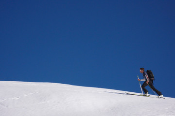 Naklejka na ściany i meble single young male back country skier hiking up a snowy ridge of a mountain in the Swiss Alps near Sargans in winter underneath a clear blue sky