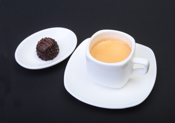 White cup of classic espresso coffee and pralines on black background.