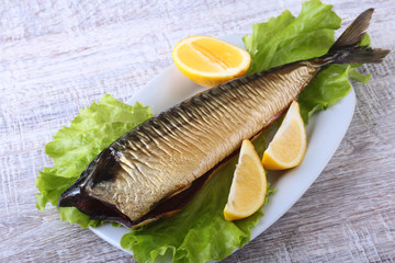 Smoked mackerele and lemon on green lettuce leaves on Wooden cutting board isolated on white background.