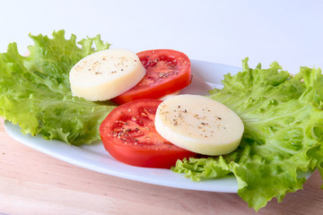 Portion of Mozzarella with Tomatoes, lettuce leaf and Balsamic dressing on white plate. selective focus close-up shot.