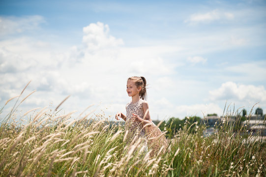 Happy child in a dress in the middle of a field of spikelets
