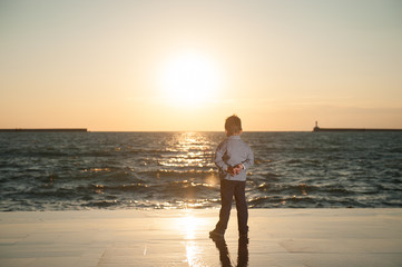 thinking little boy looking at the sea on the background of beautiful sea sunset