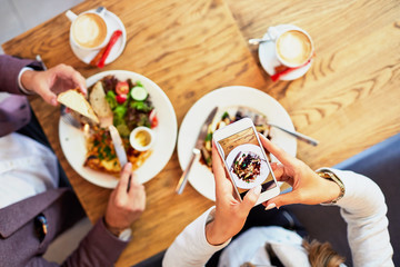 Couple of young people taking photo of their food while eating breakfast in a cafe before going to work