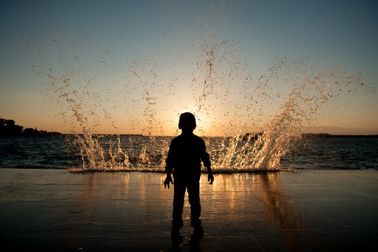 one little child watching at giant wave at beautiful ocean sunset in California
