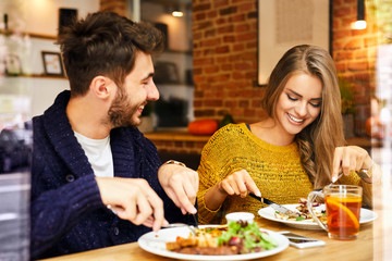 Cheerful cute young couple laughing and eating lunch together in a cafeteria