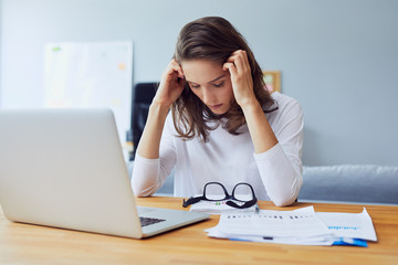 Beautiful stressed young entrepreneur holding her head and looking down stress and headache in...