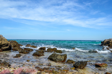 Fototapeta na wymiar blue sea wave splashing on spectacular rock in beautiful sea to make a foam with blue sky background