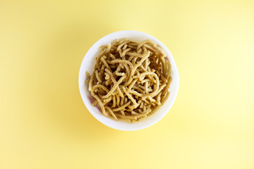 Traditional Indian Snacks on white bowl on yellow background