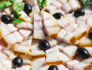Pork lard, cut into pieces on a plate, topped with olives and parsley.