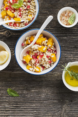 A healthy modern snack or lunch. Two bowls with pearl barley salad with slices of baked pumpkin and pomegranate seeds with butter dressing sauce. Top View.