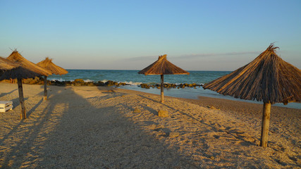 Umbrellas made of straw on the beach by the sea. Sunset. Lifestyle, relaxing summer beach at the beach resort. Vacation and travel concept summer. Horizontal photo