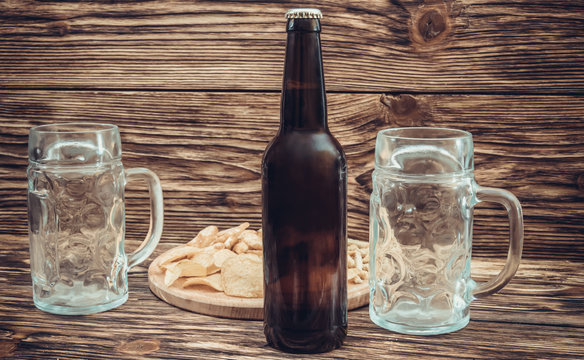Bottle of beer with two glasses and salty snacks on the wooden background. Toned.