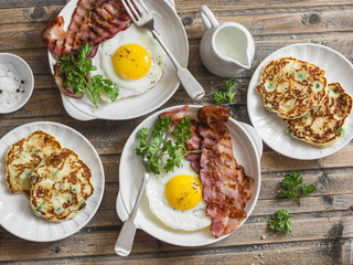 Full breakfast table - fried eggs with bacon and potatoes, green peas, leek pancakes on a wooden table, top view