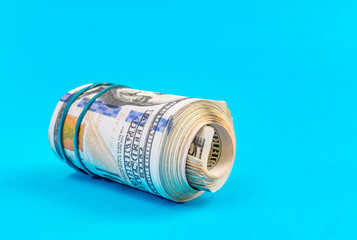 US one hundred dollar bills rolled up with rubber band on a blue.