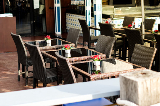 Many black rattan chairs with red rose in vase and clear table set on wooden floor at restaurant for street food background or texture - outdoor concept.