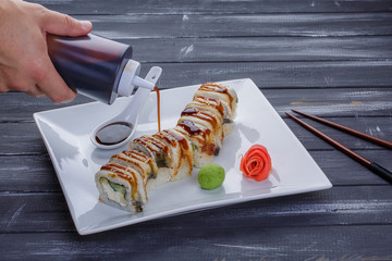 Bottle pouring sauce onto sushi. Squeeze bottle in man's hand. Japan sends greetings. Uramaki rolls from sushi cafe.