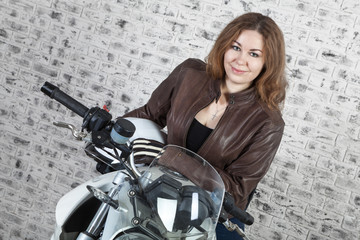 Fototapeta na wymiar Girl motorcyclist in a black jacket, helmet and gloves is in garage