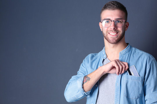 Young Man Holding A Credit Card Standing On Gray Background. Young Entrepreneur.