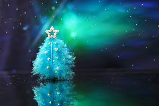 Creative layout Concept for Christmas. Beautiful Christmas tree of feathers on aurora polaris background under snowfall. Colorful bright artistic image blue and green colors. Template for text.