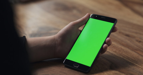 female teen girl hold smartphone with green screen over wood table
