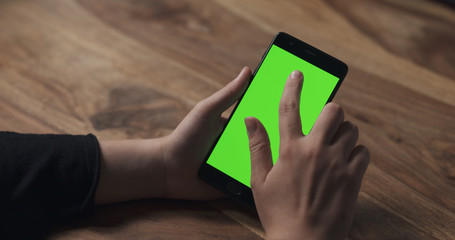female teen girl using smartphone with green screen over wood table