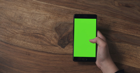 female teen girl holding smartphone with green screen over wood table