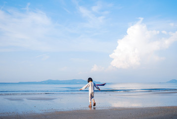 Back view of adorable little girl child play on beautiful sand beach background in summer vacation day. Natural Landscape view with happy kid.
